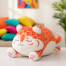 Plush toy with orange and white pattern on a light surface with colorful pillows and a plant in the background.