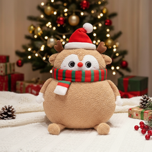 Plush reindeer toy with Santa hat and scarf in front of a Christmas tree and presents.