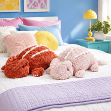 Rust Red and Blush Pink Cuddle Crest dragon plushies on a colorful bedroom bed
