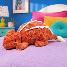 Rust Red Cuddle Crest dragon plushie on a lavender bed in a bright blue bedroom
