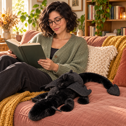 A woman reading on a sofa with the Black Dreamwing dragon plushie beside her.