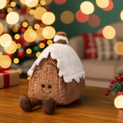 Plush gingerbread house toy with snow on top, Christmas tree, and presents in the background