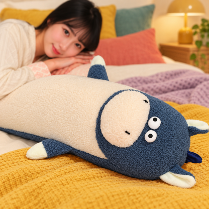 Close-up of a slate blue and cream Happy-Go-Hippo body pillow lying on mustard bedding, showing its round eyes, oval muzzle, ears, seams, and nubby plush fabric.