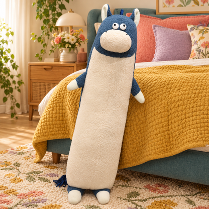 Slate blue and cream Happy-Go-Hippo plush body pillow standing upright beside a mustard bed, showing its long body, oval muzzle, small arms, feet, and tassel tail.