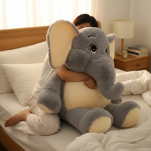 Person hugging a large plush elephant toy on a bed in a bedroom setting.