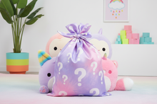 Pastel-colored plush toys with question marks on a drawstring bag in a room setting.