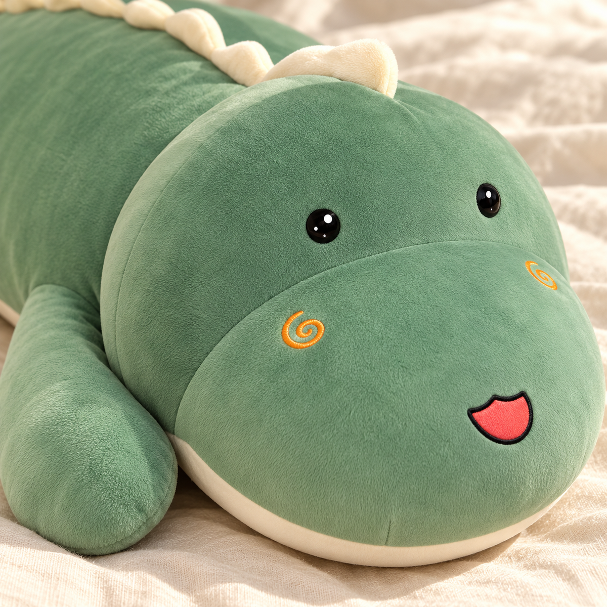 Close view of the Green dinosaur plush pillow's open eyes, spiral cheeks, smiling snout, and soft fabric.