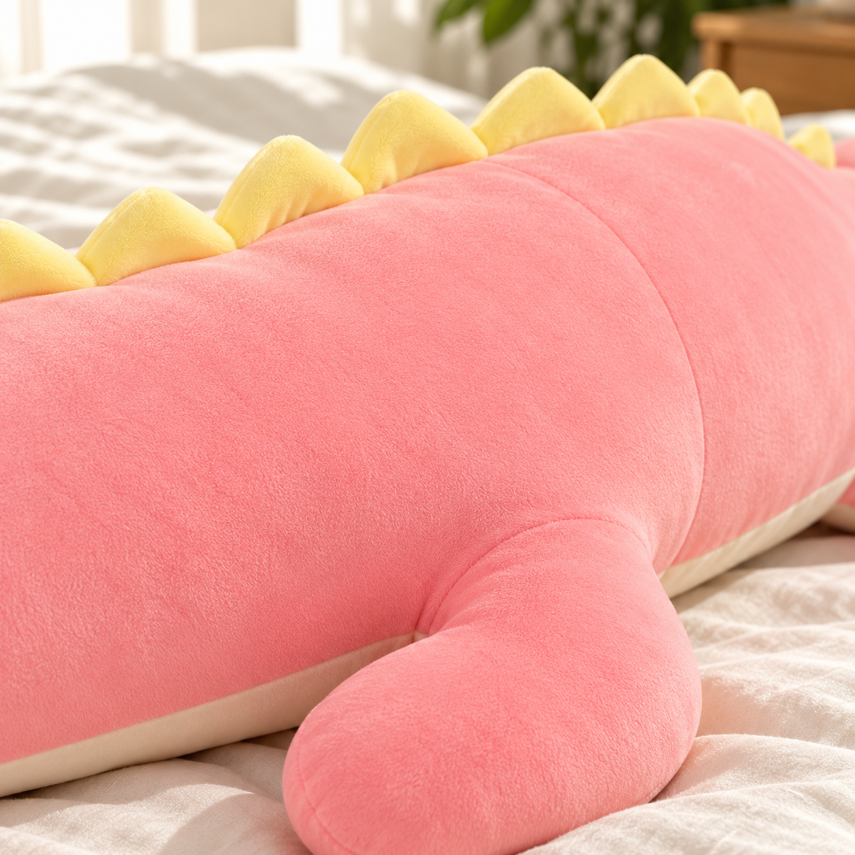 Close view of the Pink dinosaur body pillow's plush fabric, pale yellow back spines, cream underside, and floppy leg.