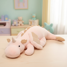 Pink dragon plush toy on a bed in a child's room with toys and furniture in the background.