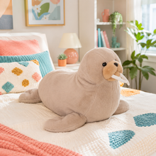 Warm taupe Wally Wobbles walrus plushie resting on a colorful bed in a bright cozy bedroom.